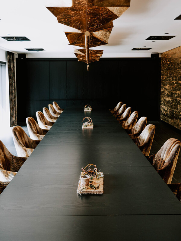 Ein langer schwarzer Konferenztisch mit braunen Stühlen und kleinen Tafelaufsätzen, unter modernen geometrischen Leuchten.