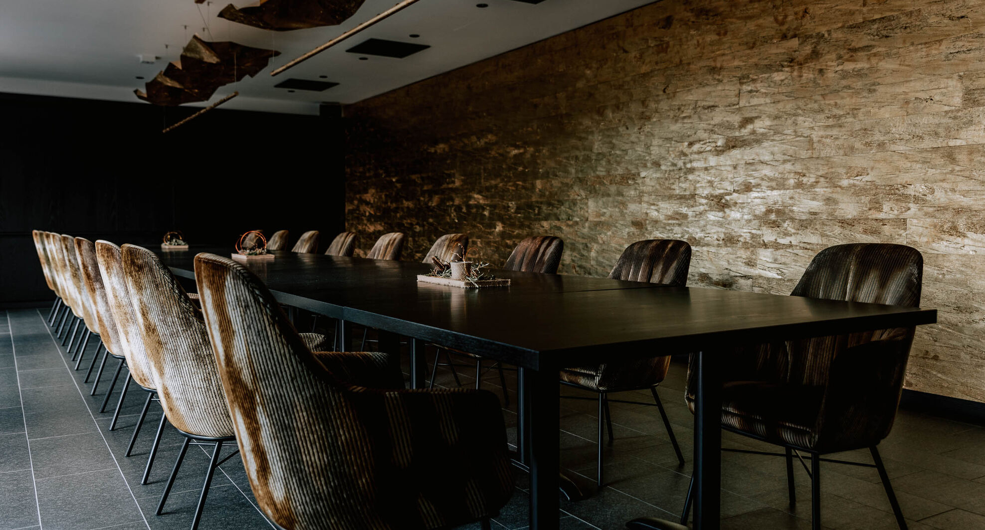 Ein moderner Konferenzraum mit einem langen schwarzen Tisch, braunen Stühlen und einer strukturierten Steinwand.