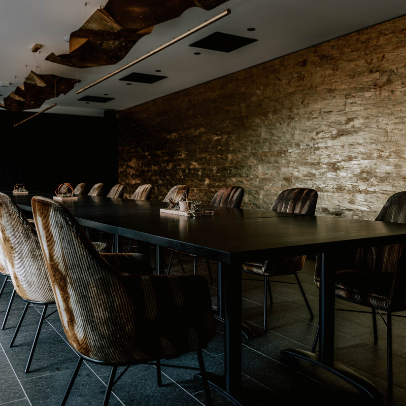Ein moderner Konferenzraum mit einem langen schwarzen Tisch, braunen Stühlen und einer strukturierten Steinwand.