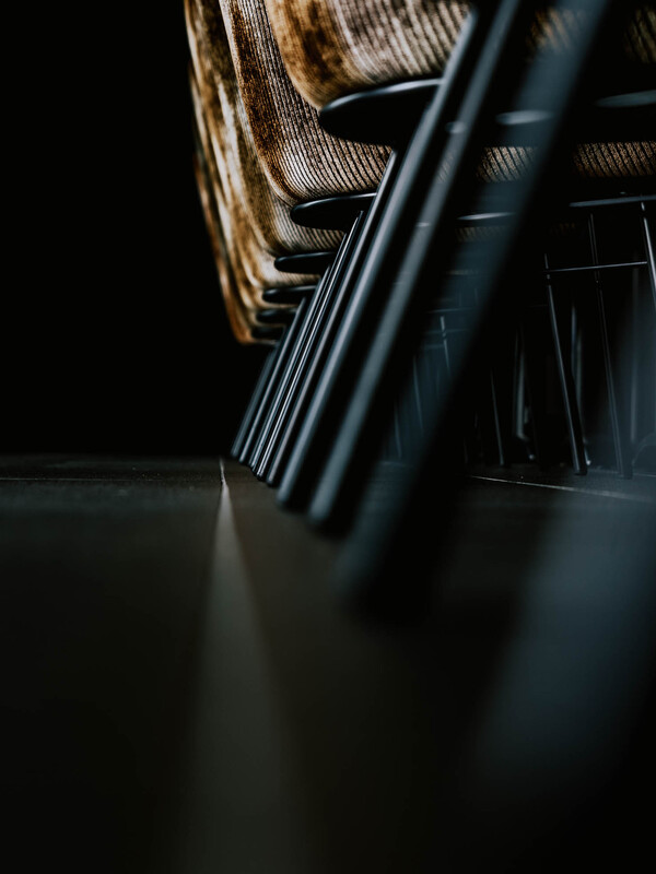 Nahaufnahme von Stuhlbeinen aus Metall in einer Reihe auf einem dunklen Boden, mit dramatischer Beleuchtung und geringer Schärfentiefe.