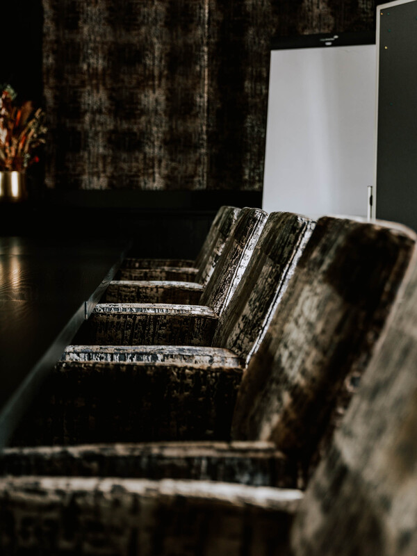 Eine Reihe von Plüschsamtstühlen an einem dunklen Konferenztisch in einem modernen, schwach beleuchteten Konferenzraum.