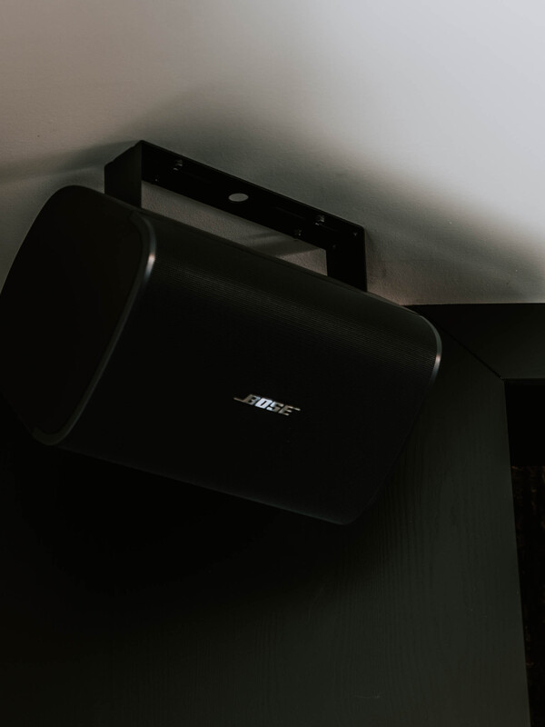 Ein schwarzer Bose-Lautsprecher, der hoch an einer dunklen Wand in der Nähe der Decke angebracht ist.