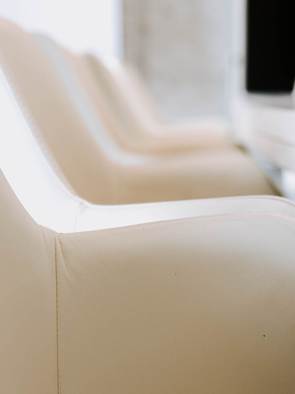 Nahaufnahme der Armlehnen mehrerer cremefarbener Stühle, die in einer Reihe angeordnet sind.