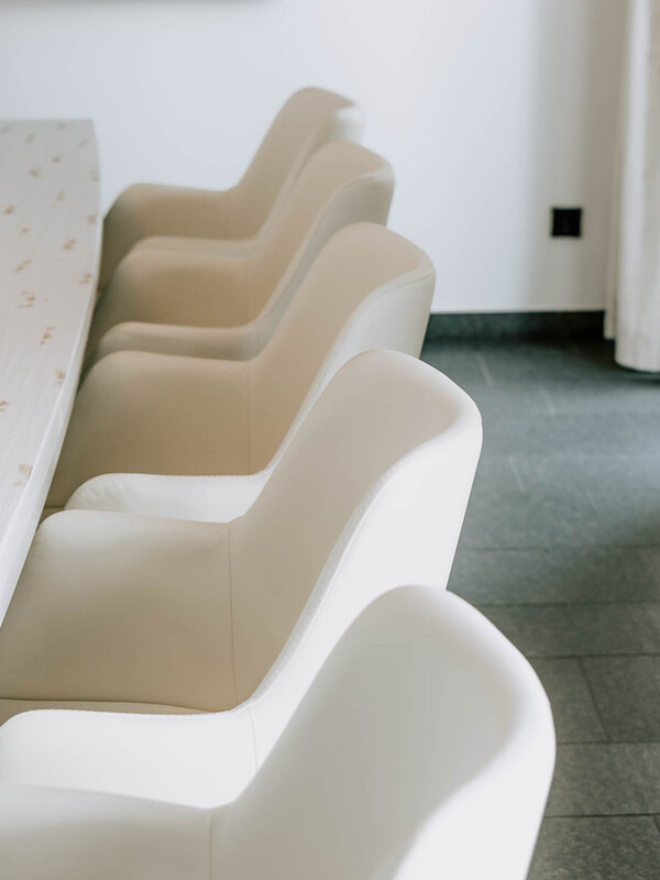 Eine Reihe moderner weißer Stühle neben einem ovalen Tisch in einem hellen, minimalistischen Raum.