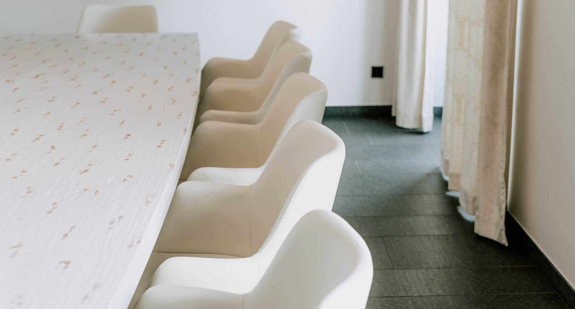 Eine Reihe moderner weißer Stühle neben einem ovalen Tisch in einem hellen, minimalistischen Raum.