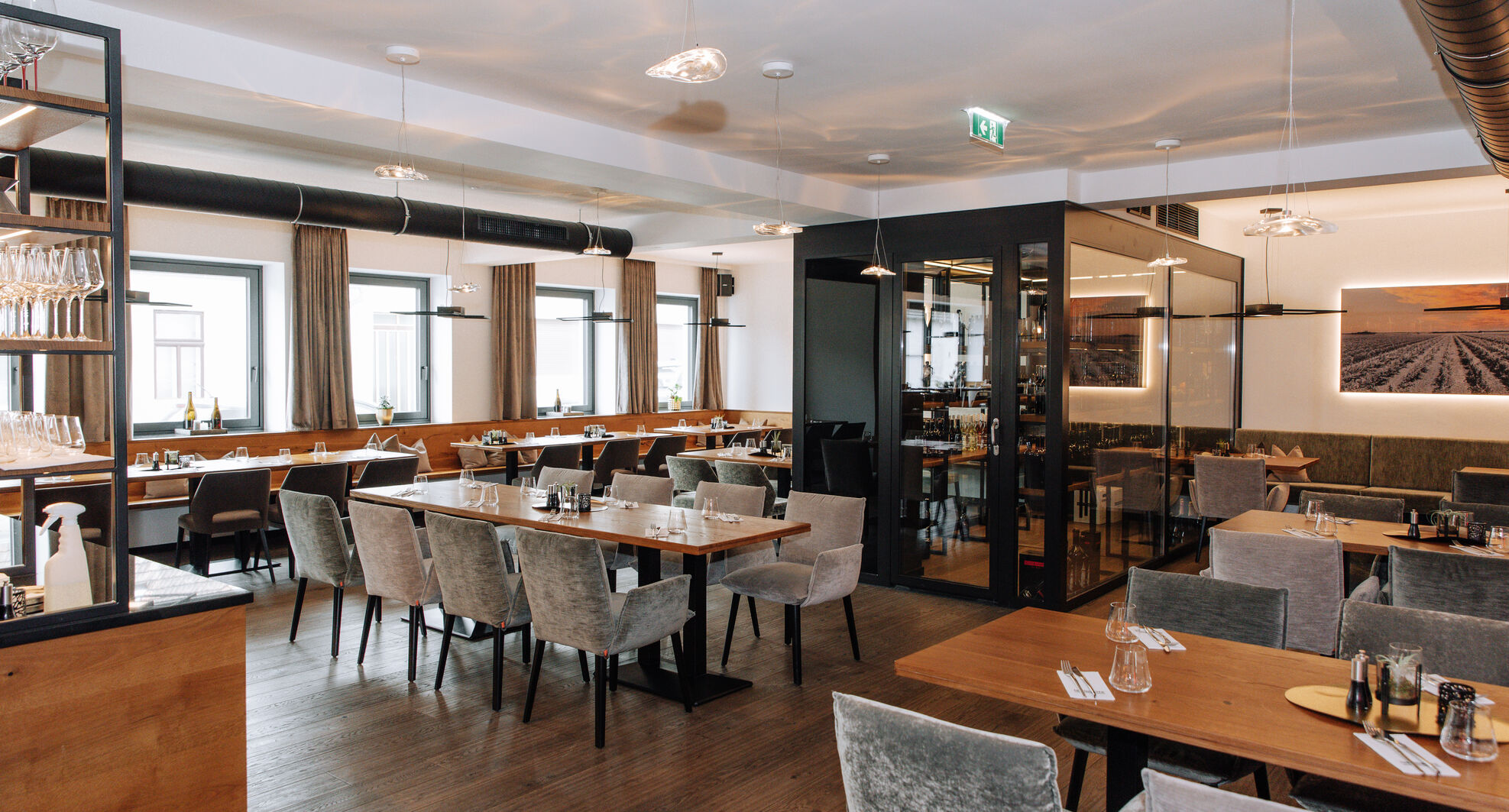 Moderner Restaurantbereich mit grauen Stühlen, Holztischen und großen Fenstern, die natürliches Licht hereinlassen.