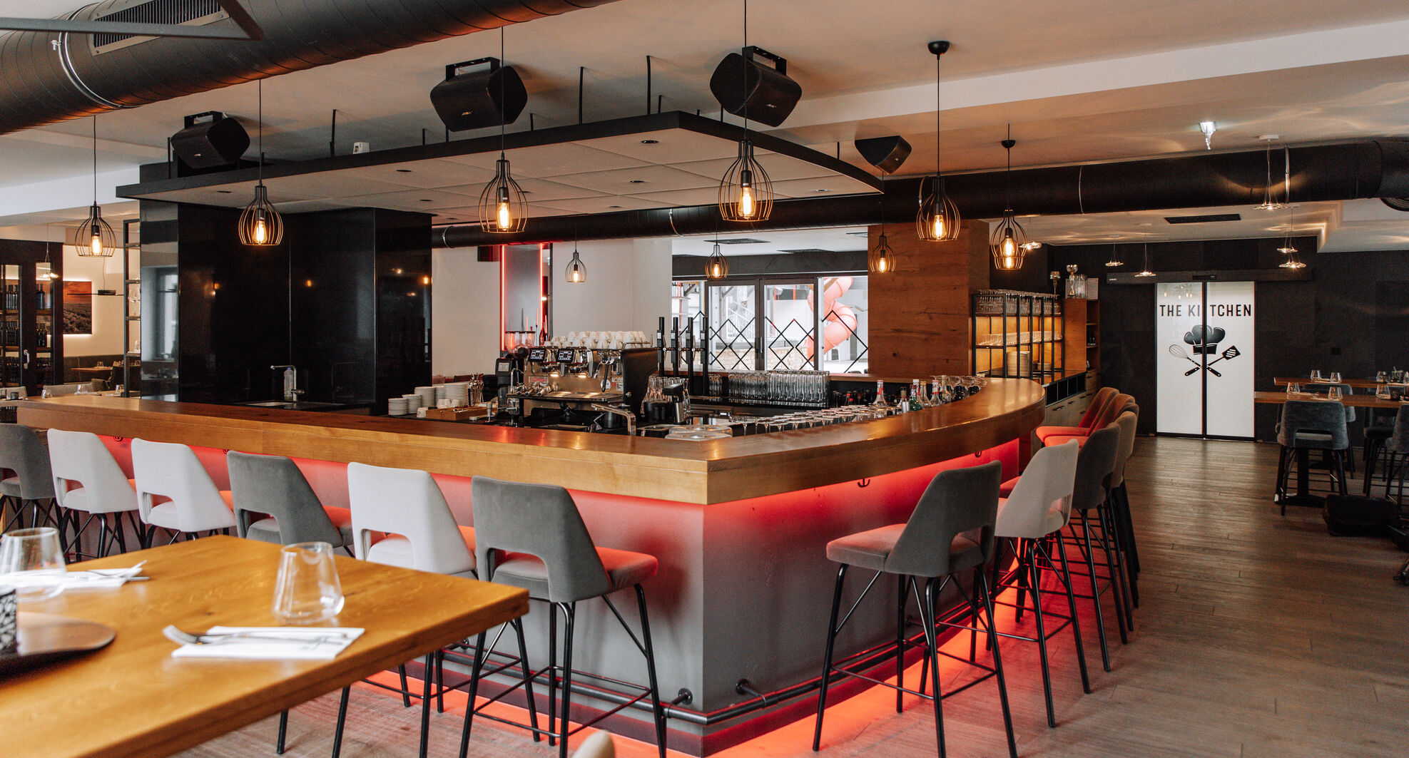 Modernes Restaurantinterieur mit zentraler Bar, hohen Stühlen, Hängelampen und einem stilvollen, warmen Ambiente.