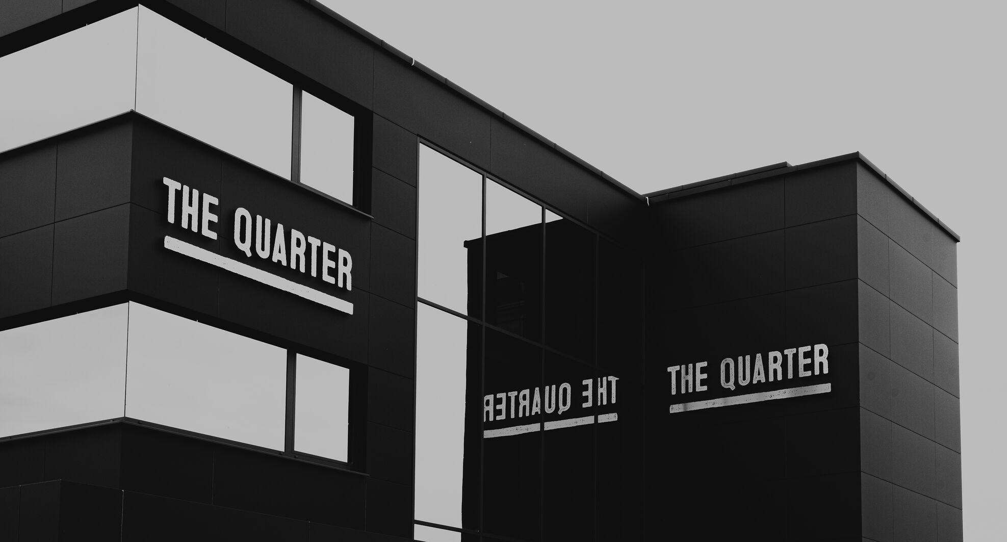 Modernes schwarzes Gebäude mit Glasfenstern und The Quarter-Schild an der Außenwand.