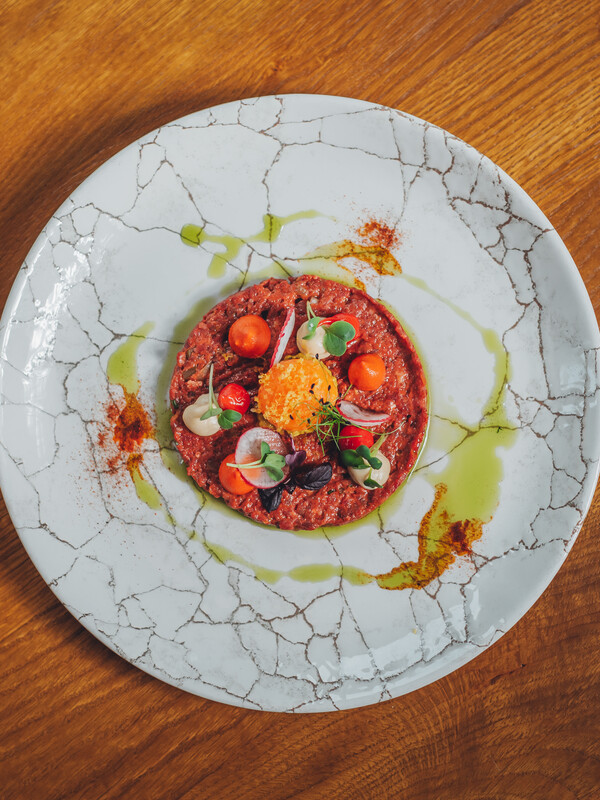 Ein Gourmet-Tartar-Gericht mit Mikrogrün, Kirschtomaten und Sauce auf einem weißen Teller mit Rissen.