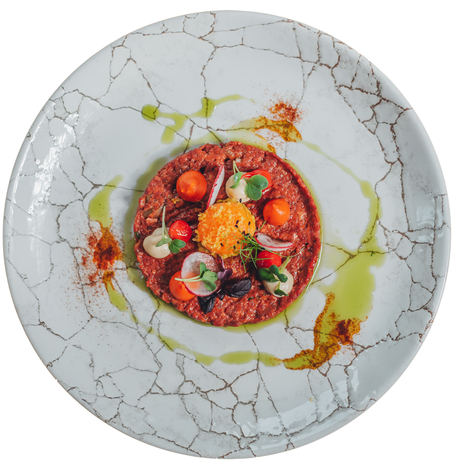 Gourmet-Steak-Tartar, garniert mit Mikrogrün, Kirschtomaten und Eigelb auf einem weißen Teller mit Riss.